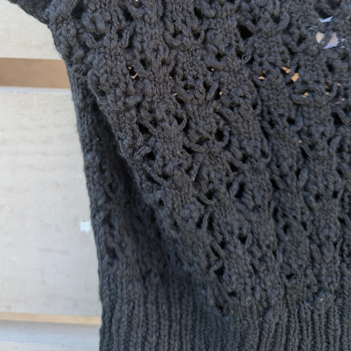 Black crocheted garment with intricate pattern on a wooden surface