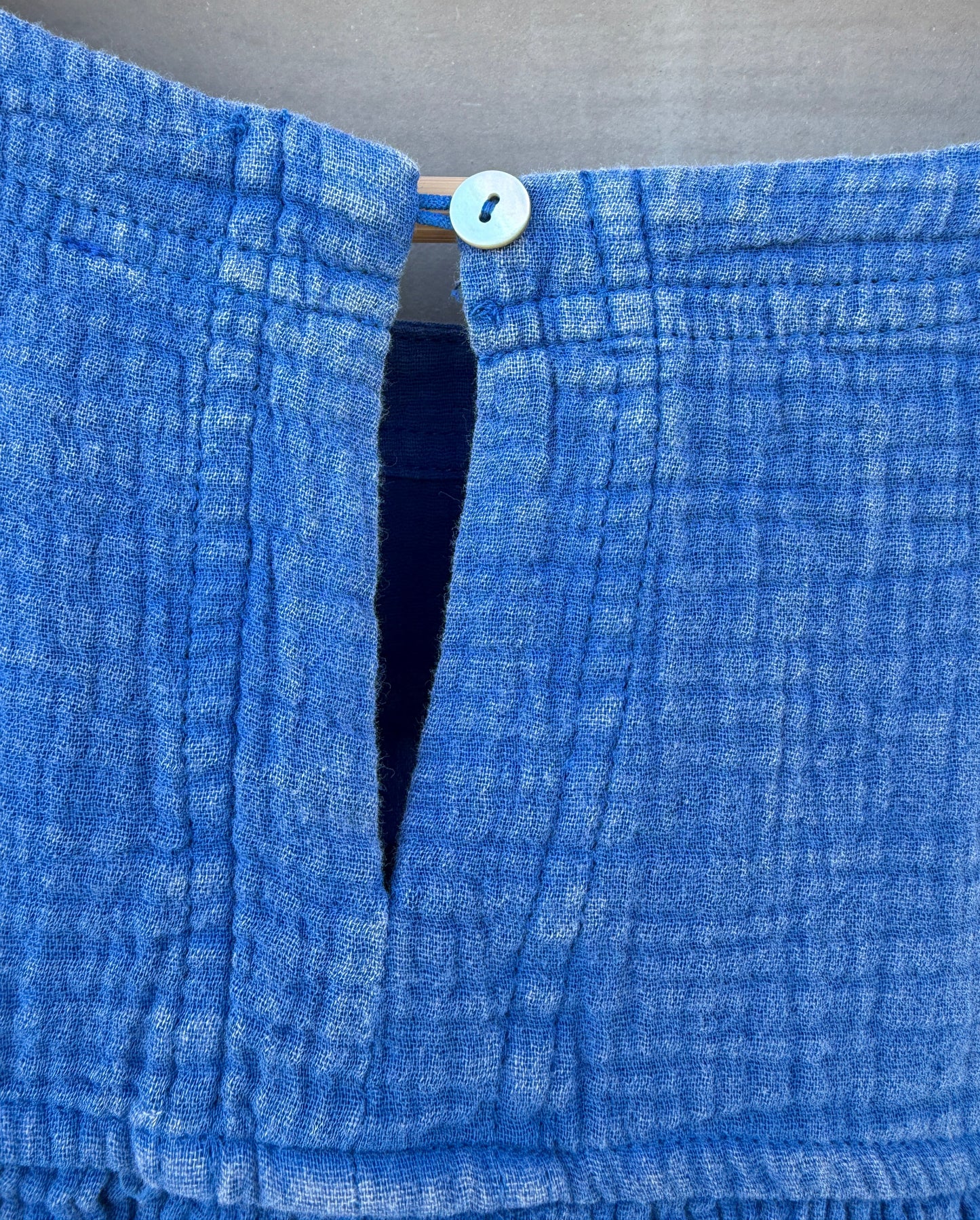 Close-up of a blue textured fabric with a button on a neutral background