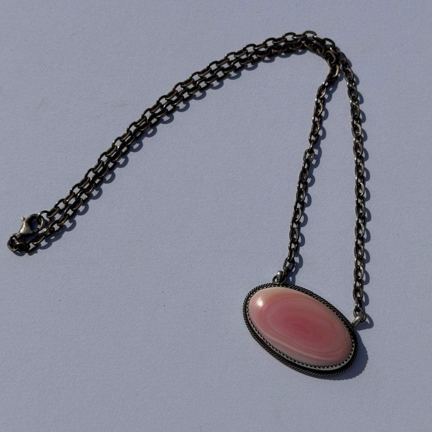 Pink oval pendant on a silver chain against a gray background