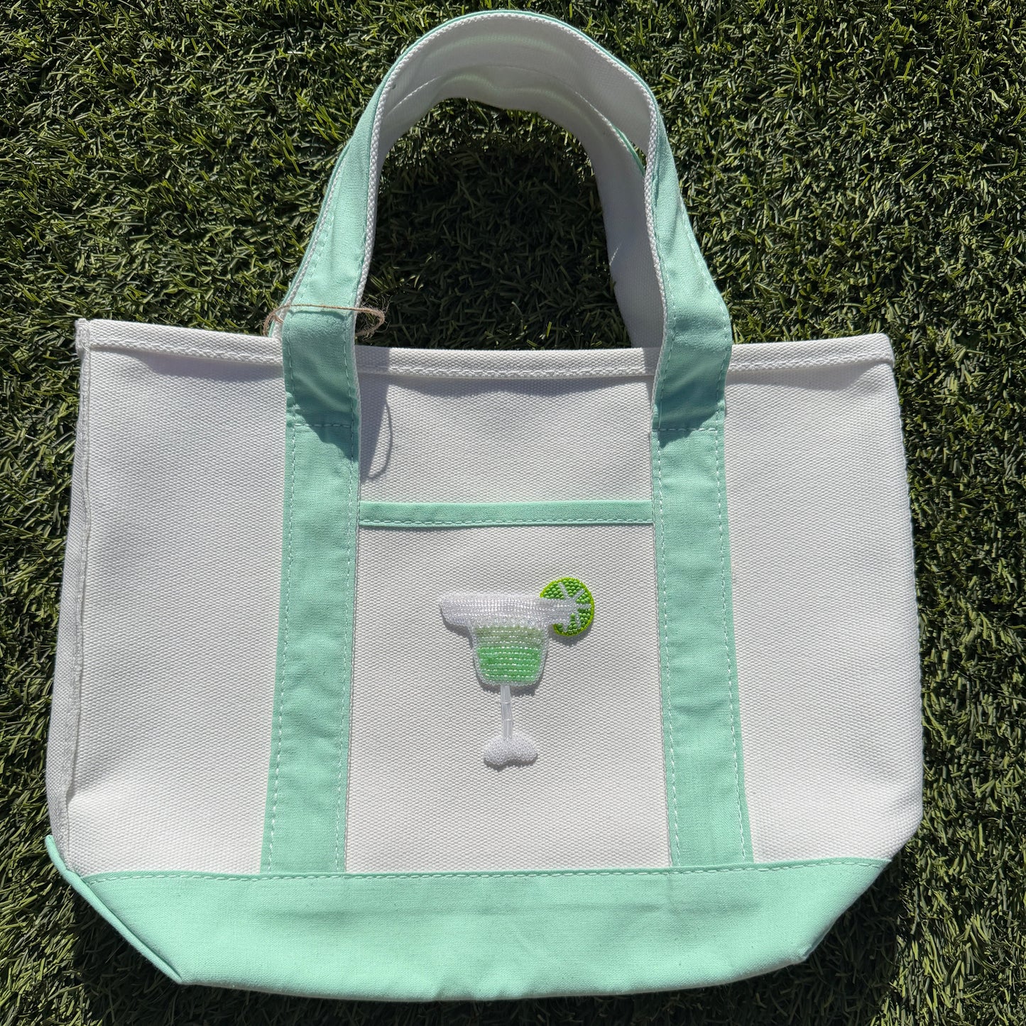 White tote bag with green accents on a grassy background