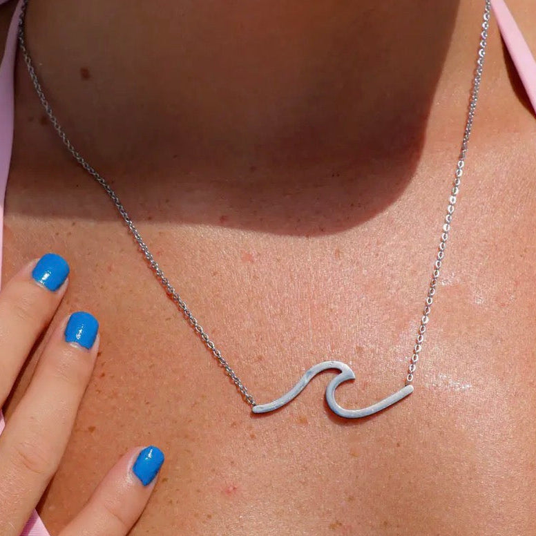 Silver wave-shaped necklace on a person wearing a pink top with blue nail polish.