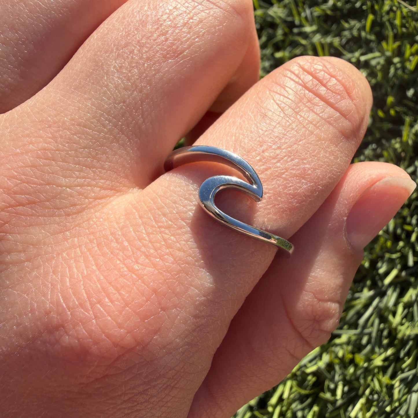 Hand wearing a silver ring with a wave design against a grassy background