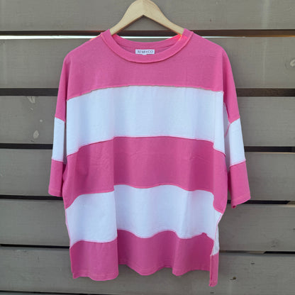 A pink and white horizontally striped short-sleeve t-shirt hanging on a wooden hanger against a gray wooden slat wall.