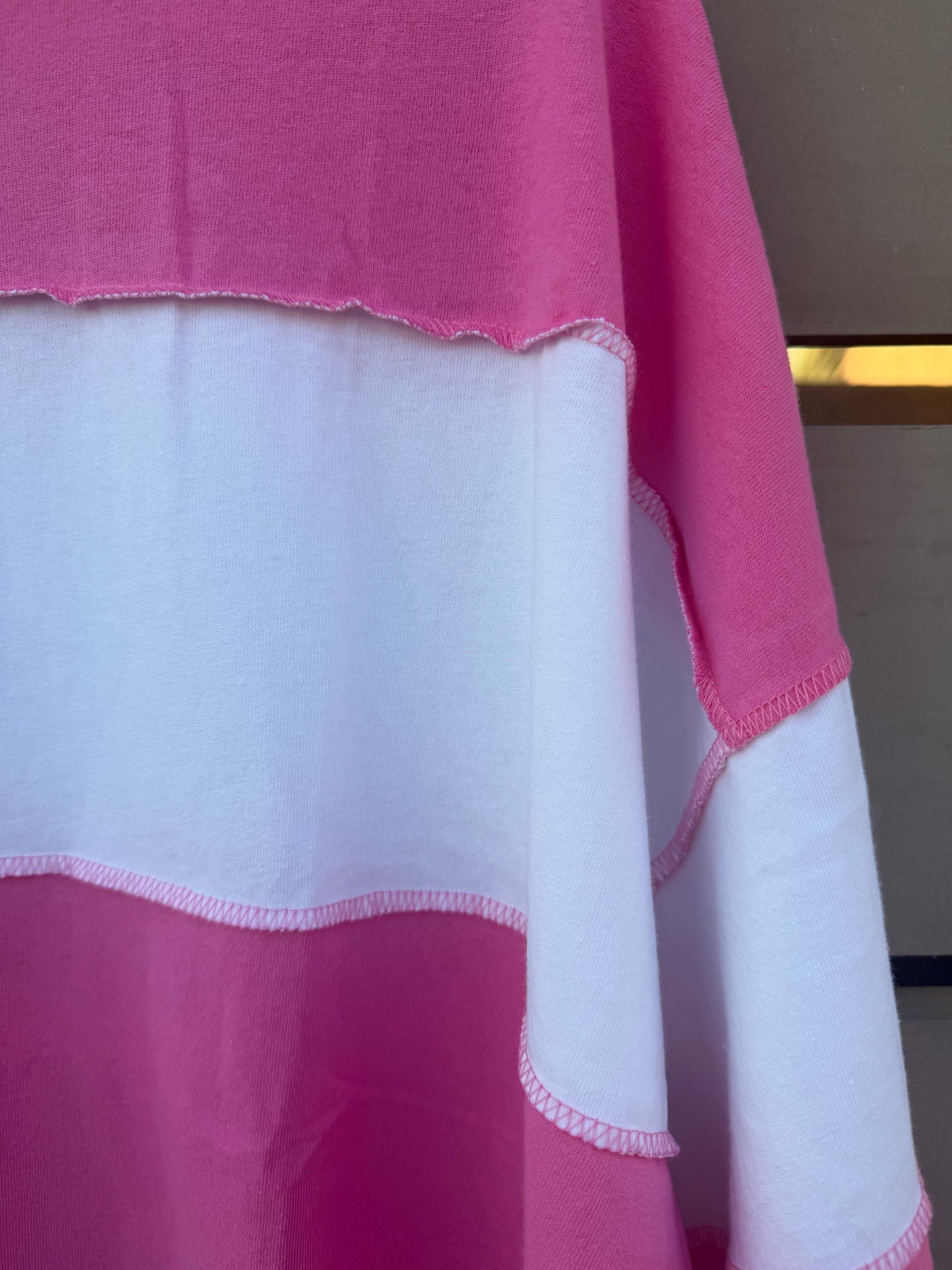 A close-up of a pink and white color-blocked fabric garment, showing the raw, scalloped edges of the material.
