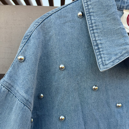 A close-up of a light blue denim jacket decorated with small silver metallic studs, showing the collar and sleeve details.
