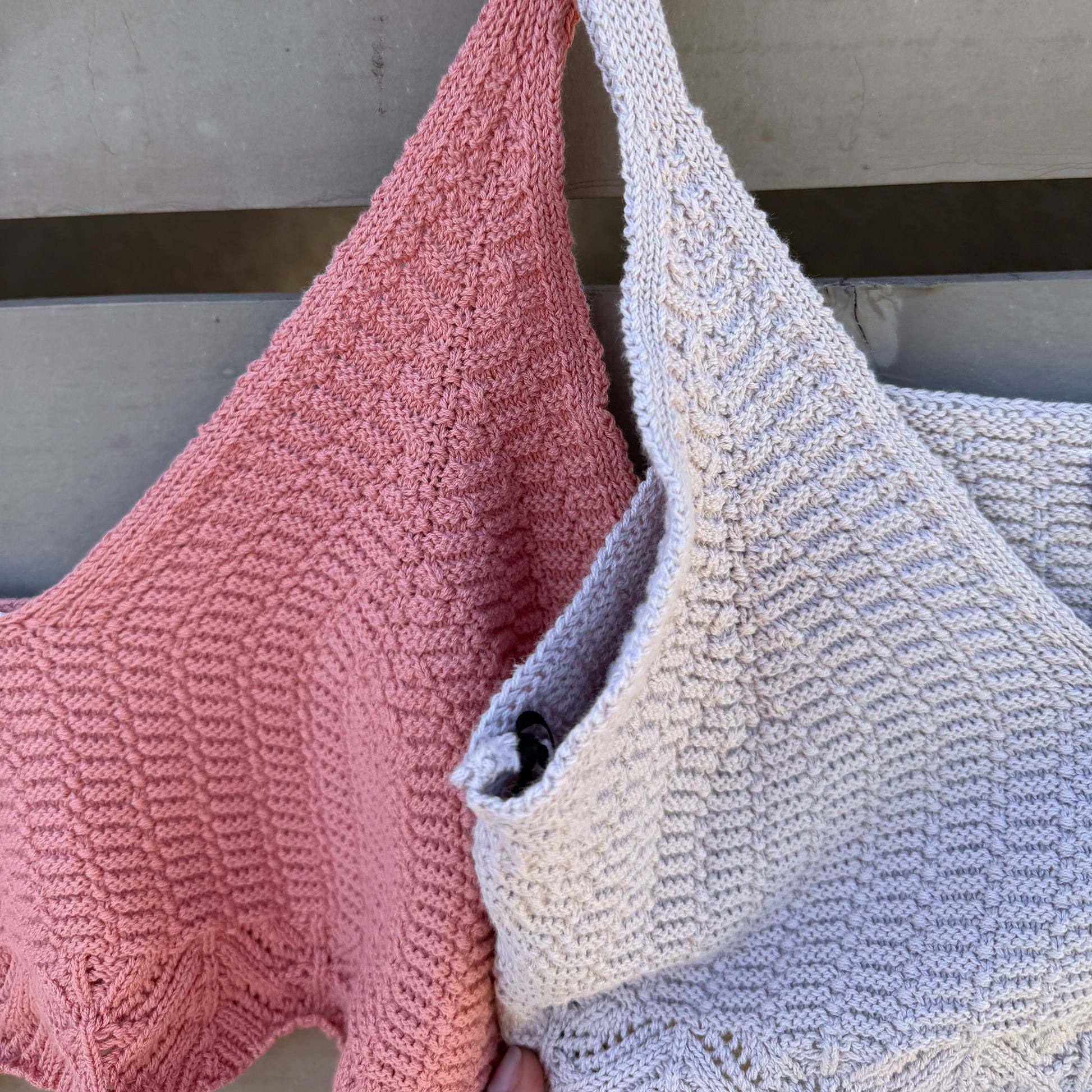 Two knitted bralettes, one pink and one purple, hanging on wooden hangers