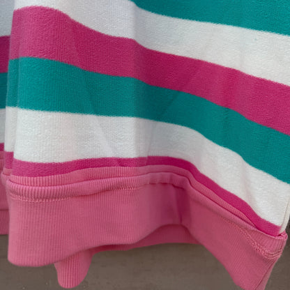 A close-up of a striped knit garment, likely a sweatshirt or sweater, featuring horizontal bands of bright pink, teal green, and white. The bottom edge shows a solid pink ribbed cuff.