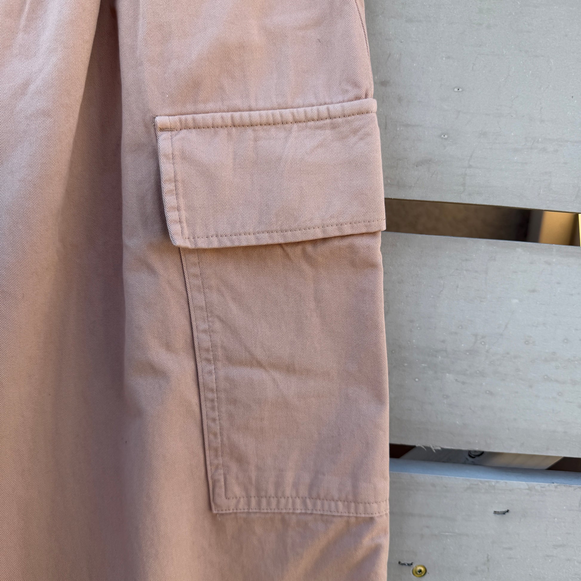 Close-up of a beige jacket with a pocket, hanging on a metal rack.
