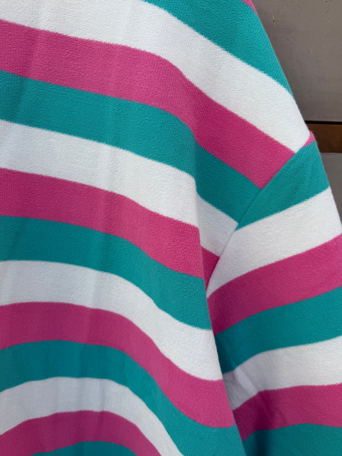 A close-up of a striped knit fabric with alternating horizontal bands of teal green, magenta pink, and white.