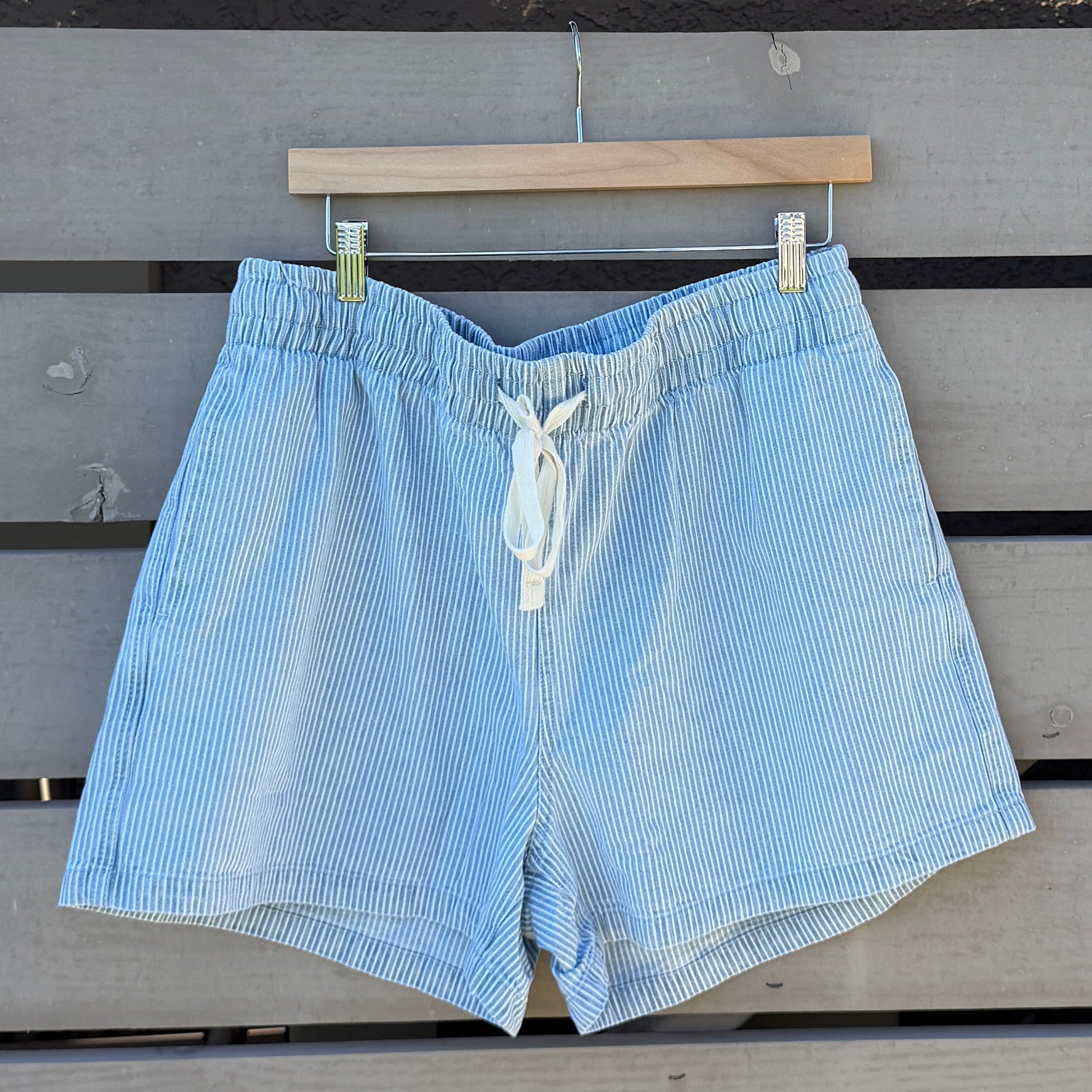 Light blue shorts hanging on a wooden hanger against a wooden slat wall.