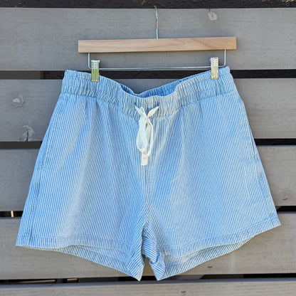 Light blue shorts hanging on a wooden hanger against a wooden slat wall.