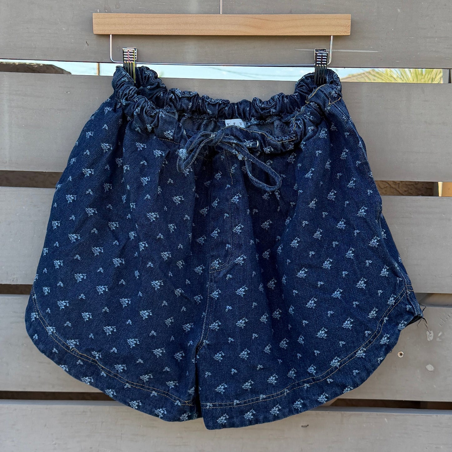 Blue denim shorts hanging on a wooden slatted structure with a clear blue sky background