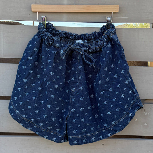Blue denim shorts hanging on a wooden slatted structure with a clear blue sky background