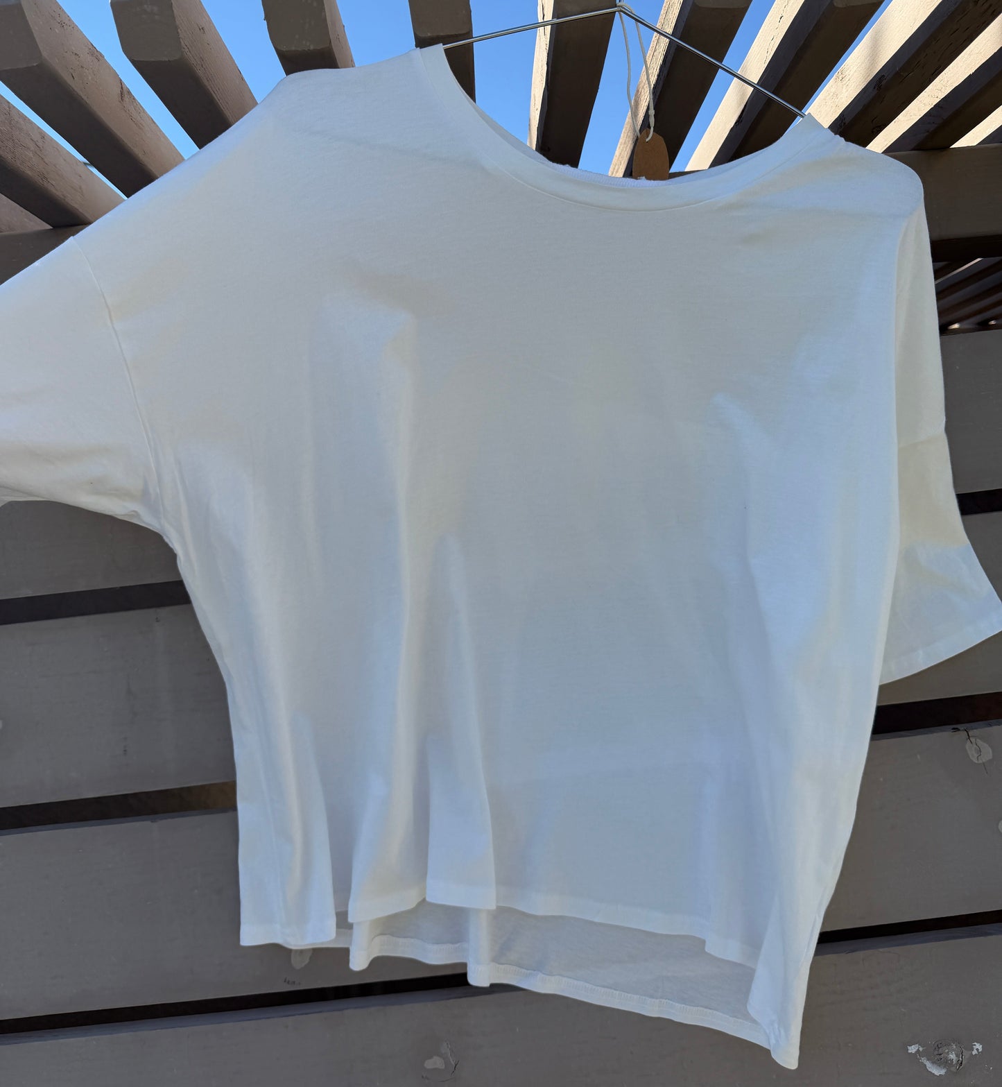White t-shirt hanging on a wooden surface with a blue sky background