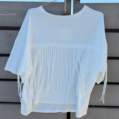 White fringe top hanging on a wooden surface