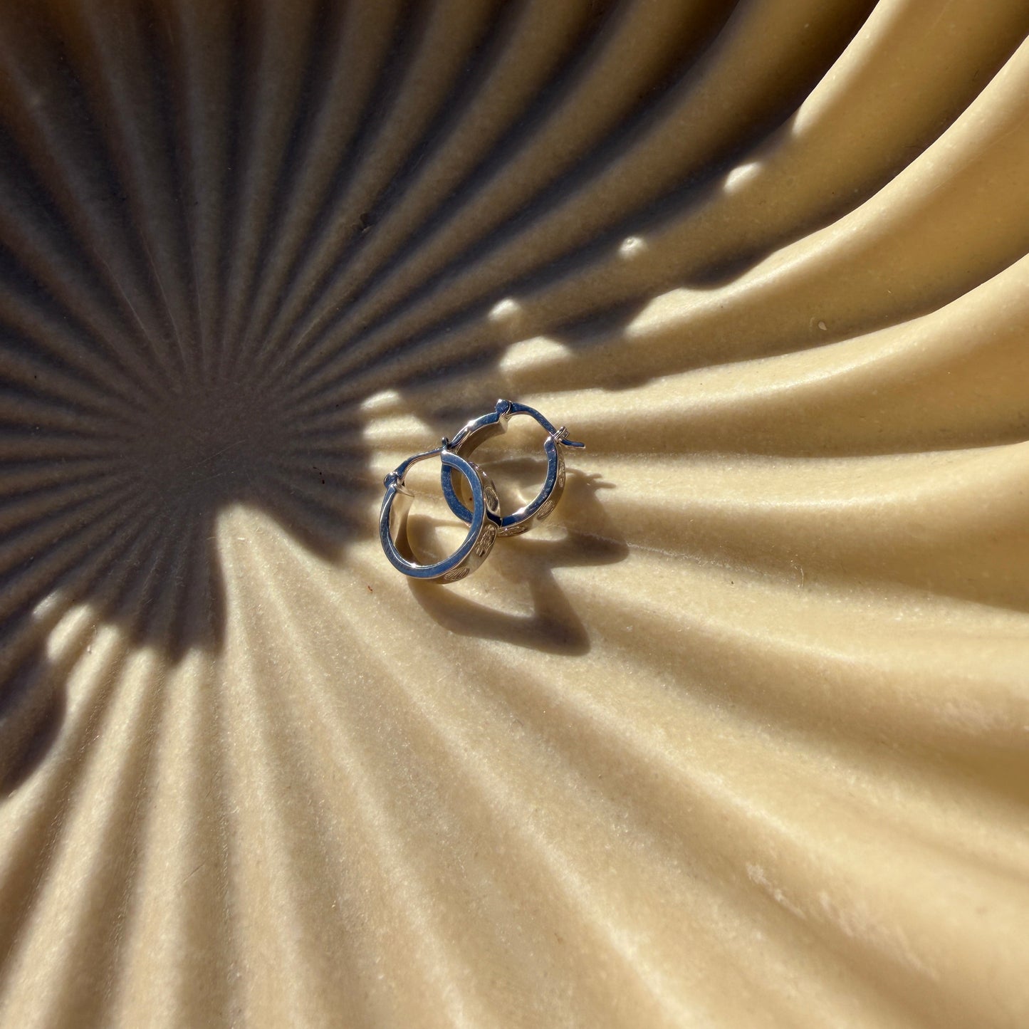 Two silver earrings on a textured beige surface