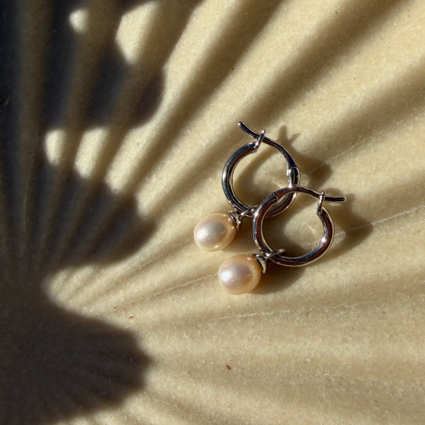 Pair of hoop earrings with pearl accents on a textured beige surface