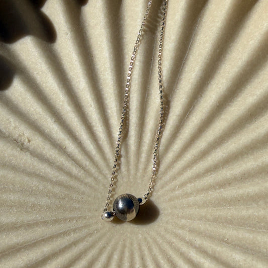 Close-up of a necklace with a pendant on a textured beige surface