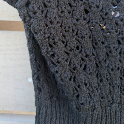 Black crocheted garment with intricate pattern on a wooden surface