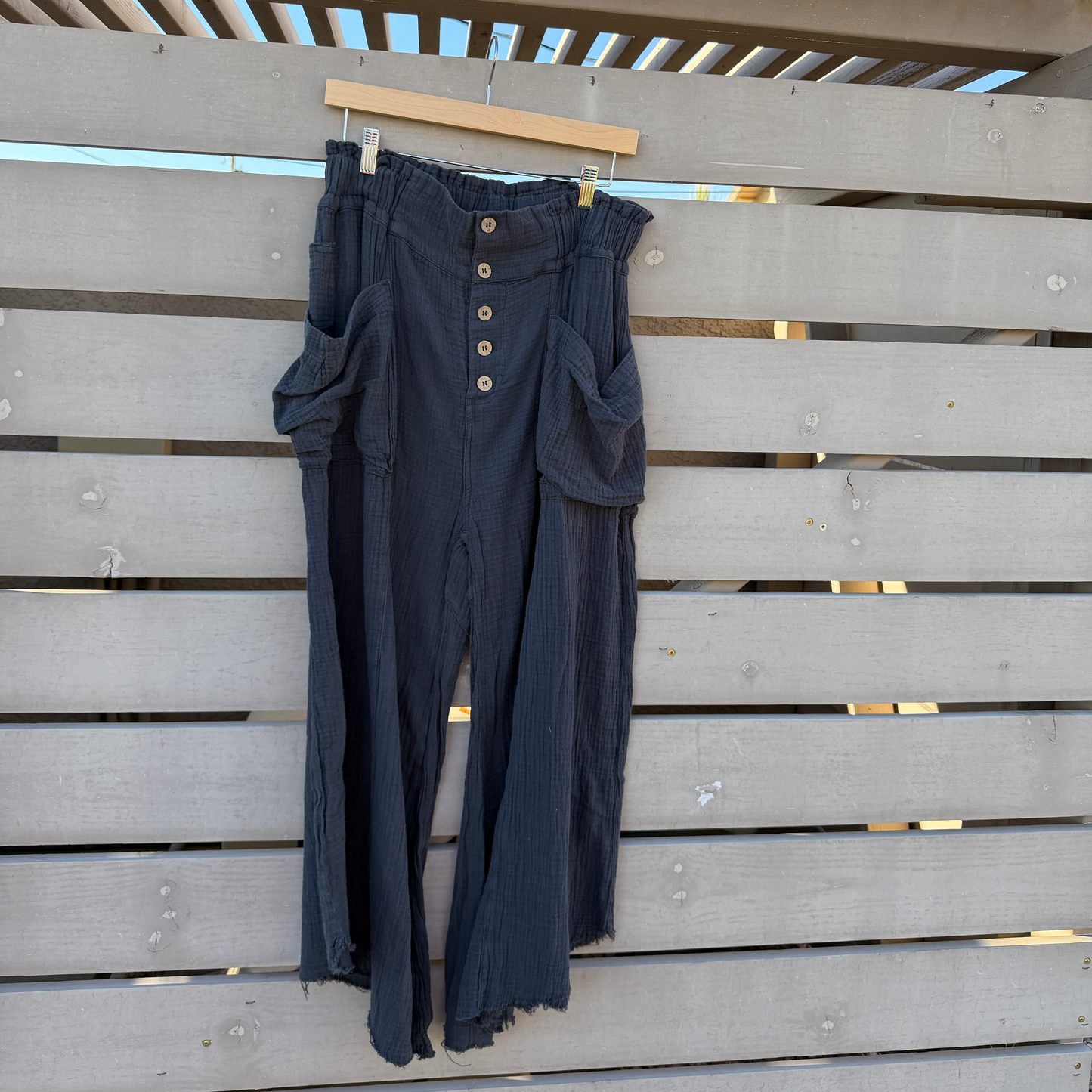 Dark black pants with buttons hanging on a wooden fence