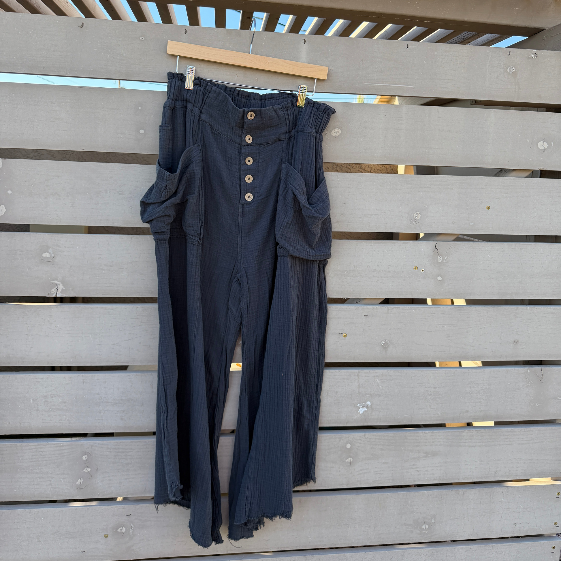 Dark black pants with buttons hanging on a wooden fence