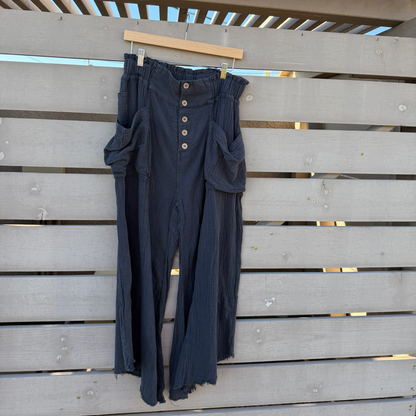 Dark black pants with buttons hanging on a wooden fence