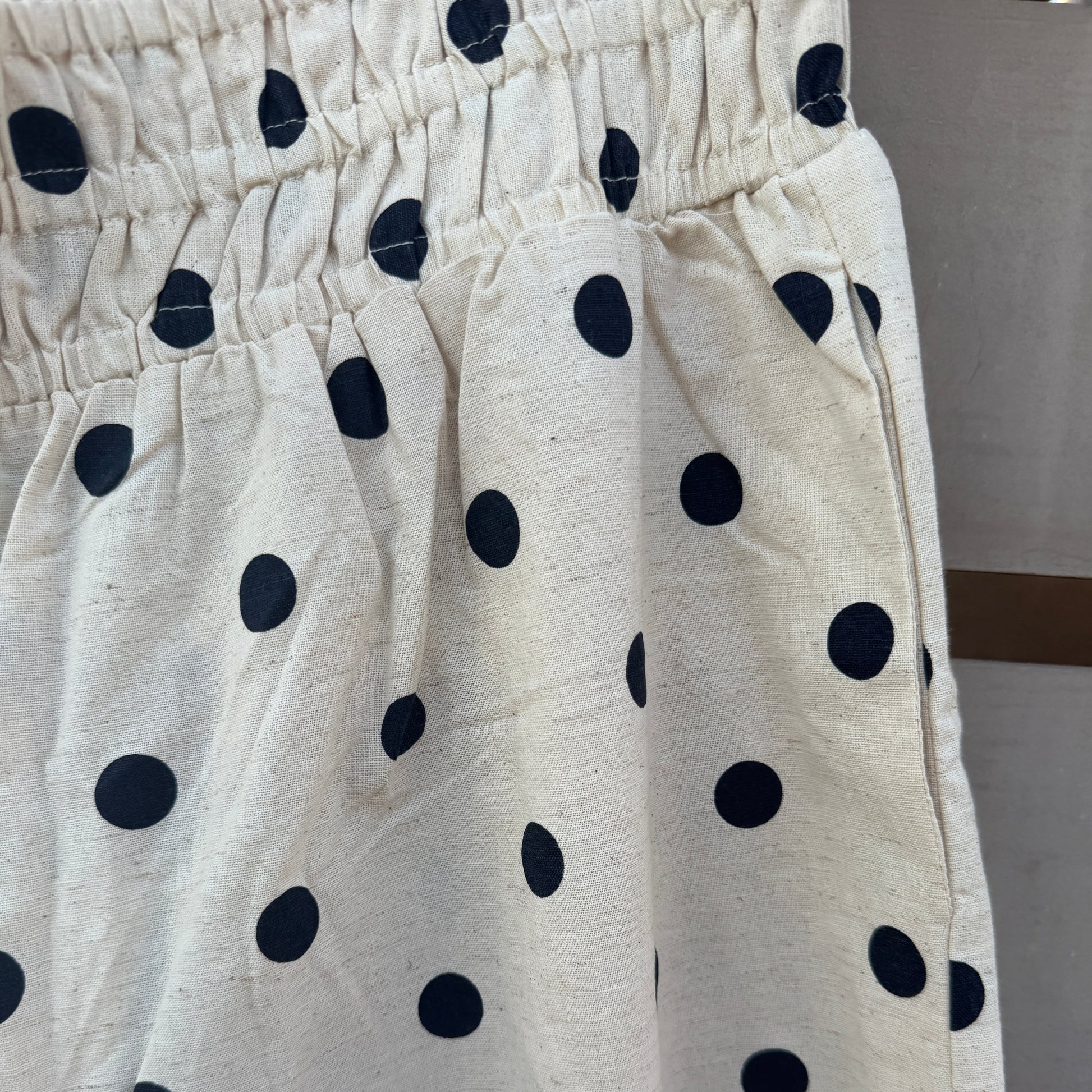Close-up of a cream-colored fabric garment with a black polka dot pattern and an elastic waistband.
