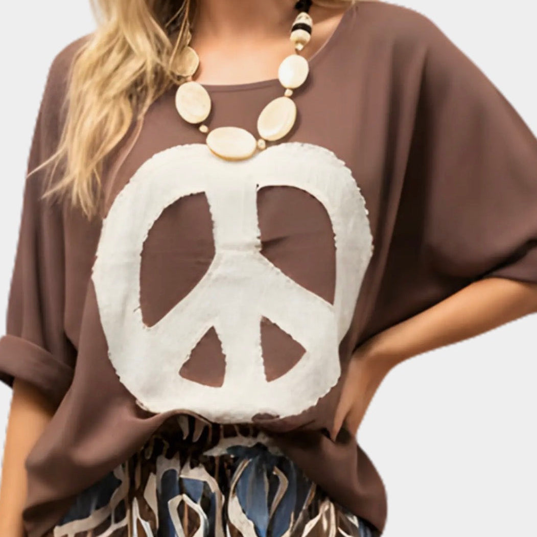 Person wearing a brown shirt with a white peace symbol design on a plain background