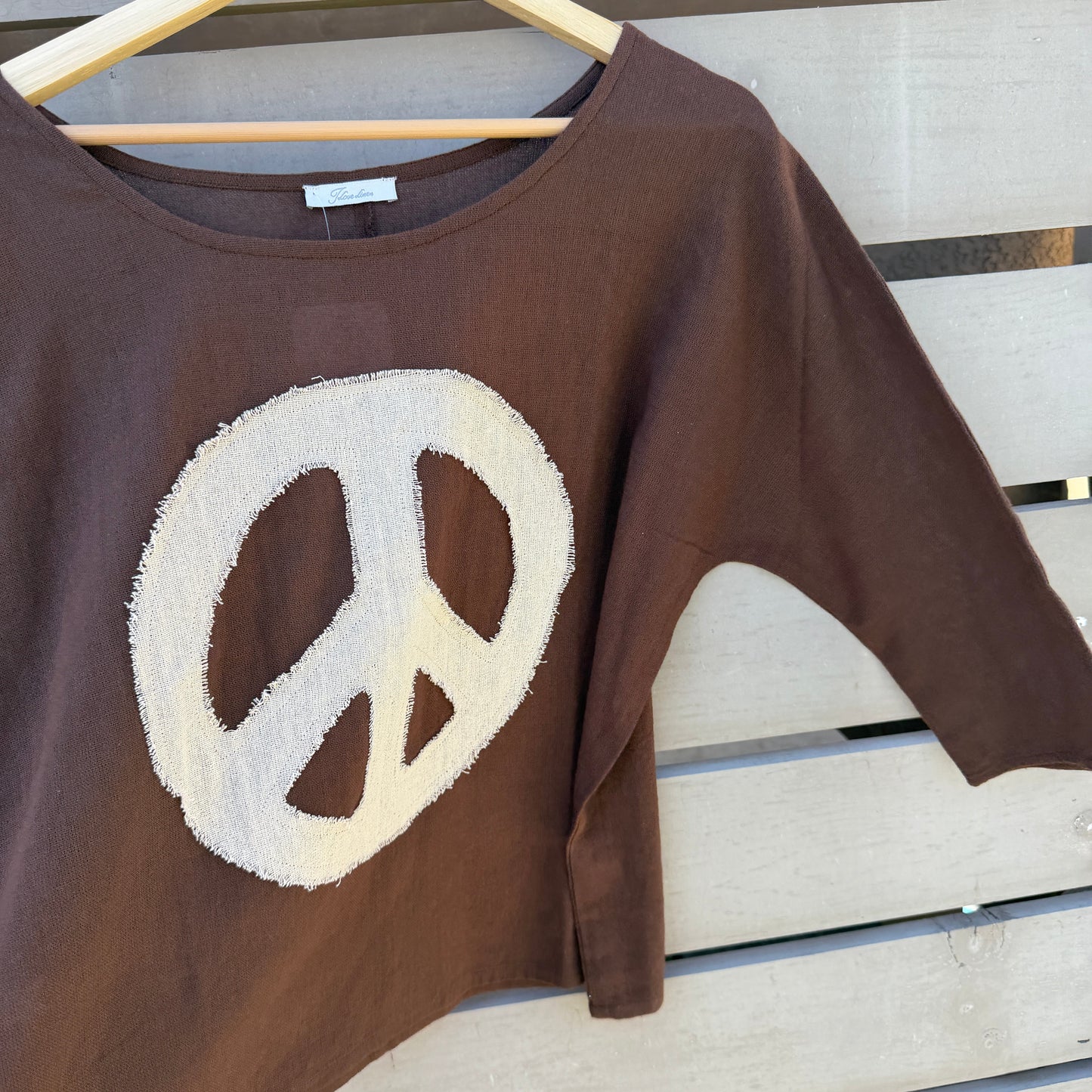 Brown shirt with a peace symbol on a wooden hanger against a wooden background
