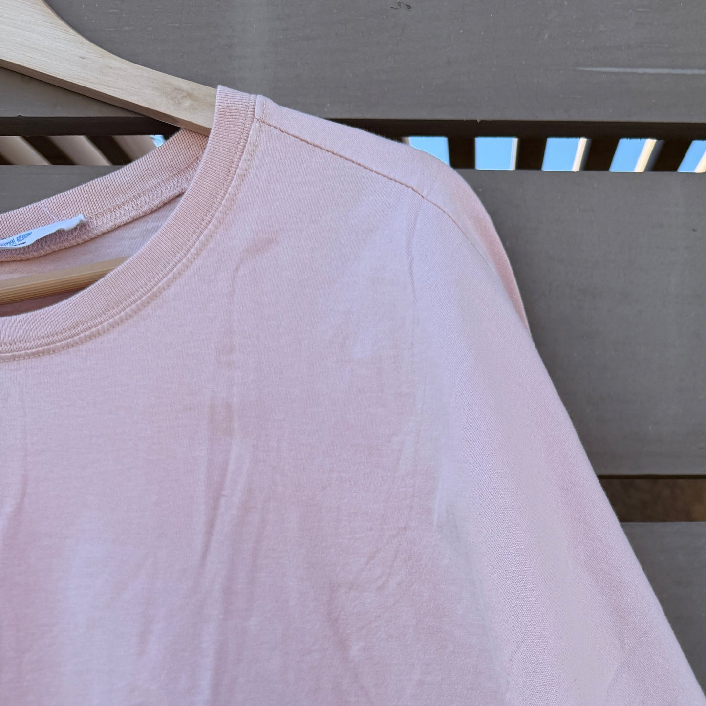 Pink t-shirt on a wooden hanger against a gray wall.