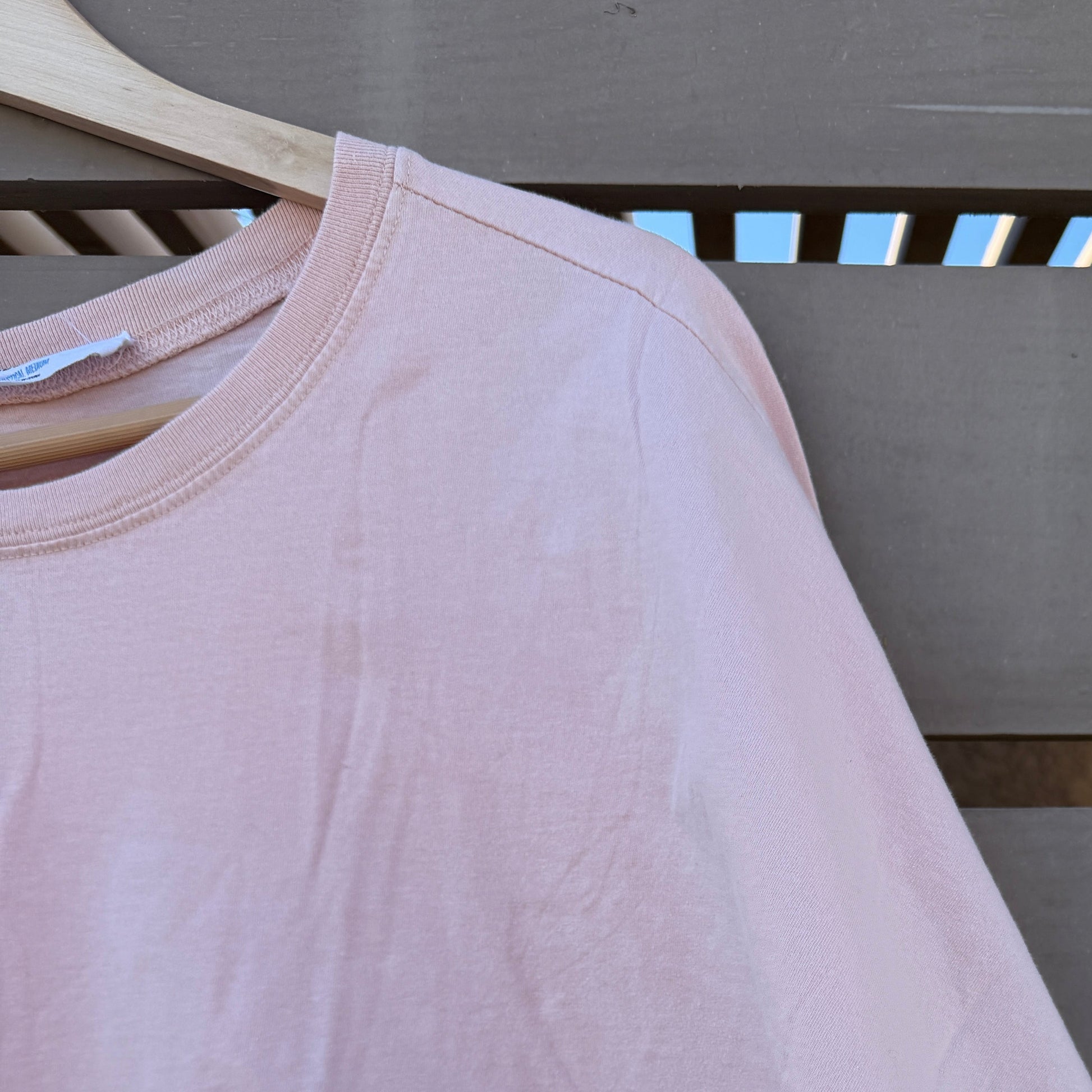 Pink t-shirt on a wooden hanger against a gray wall.
