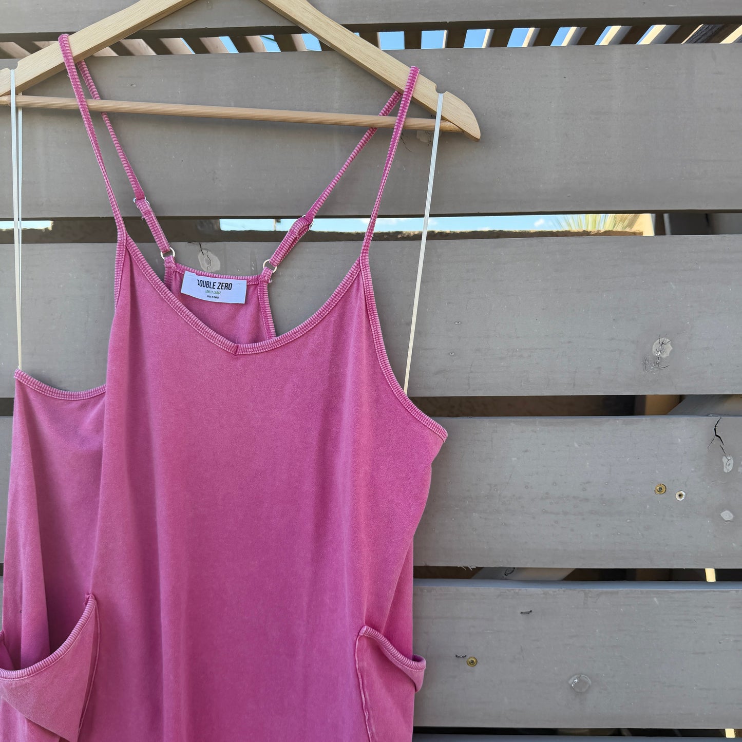 Pink jumpsuit on a hanger against a wooden panel background
