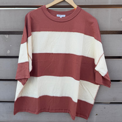 A short-sleeve striped t-shirt with horizontal bands of rust red and cream, hanging on a wooden hanger against a gray wooden slat wall.
