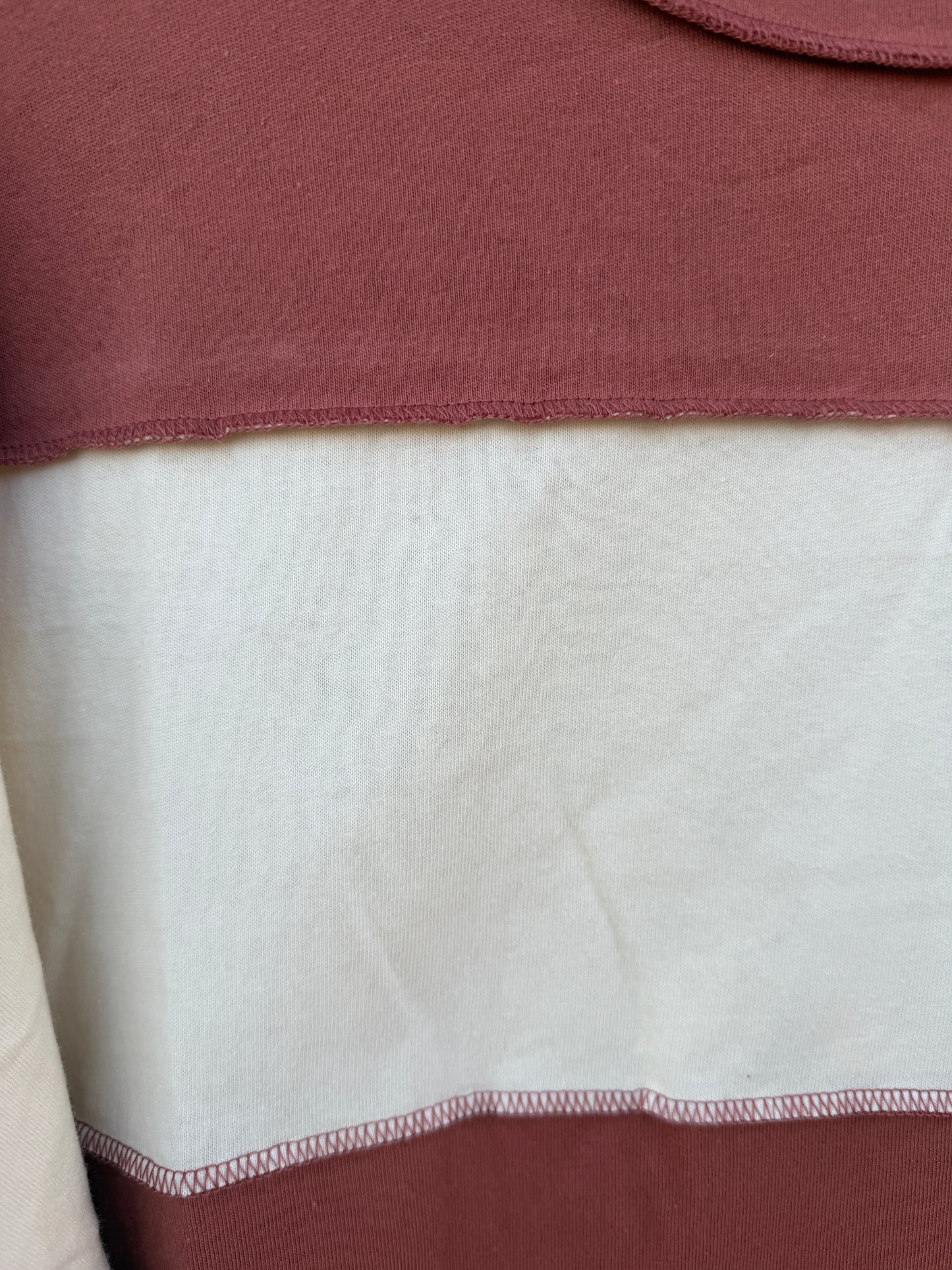 Close-up of a color-blocked garment showing a dusty rose/mauve top section, a large off-white central panel, and a darker mauve bottom section with visible stitched seams.