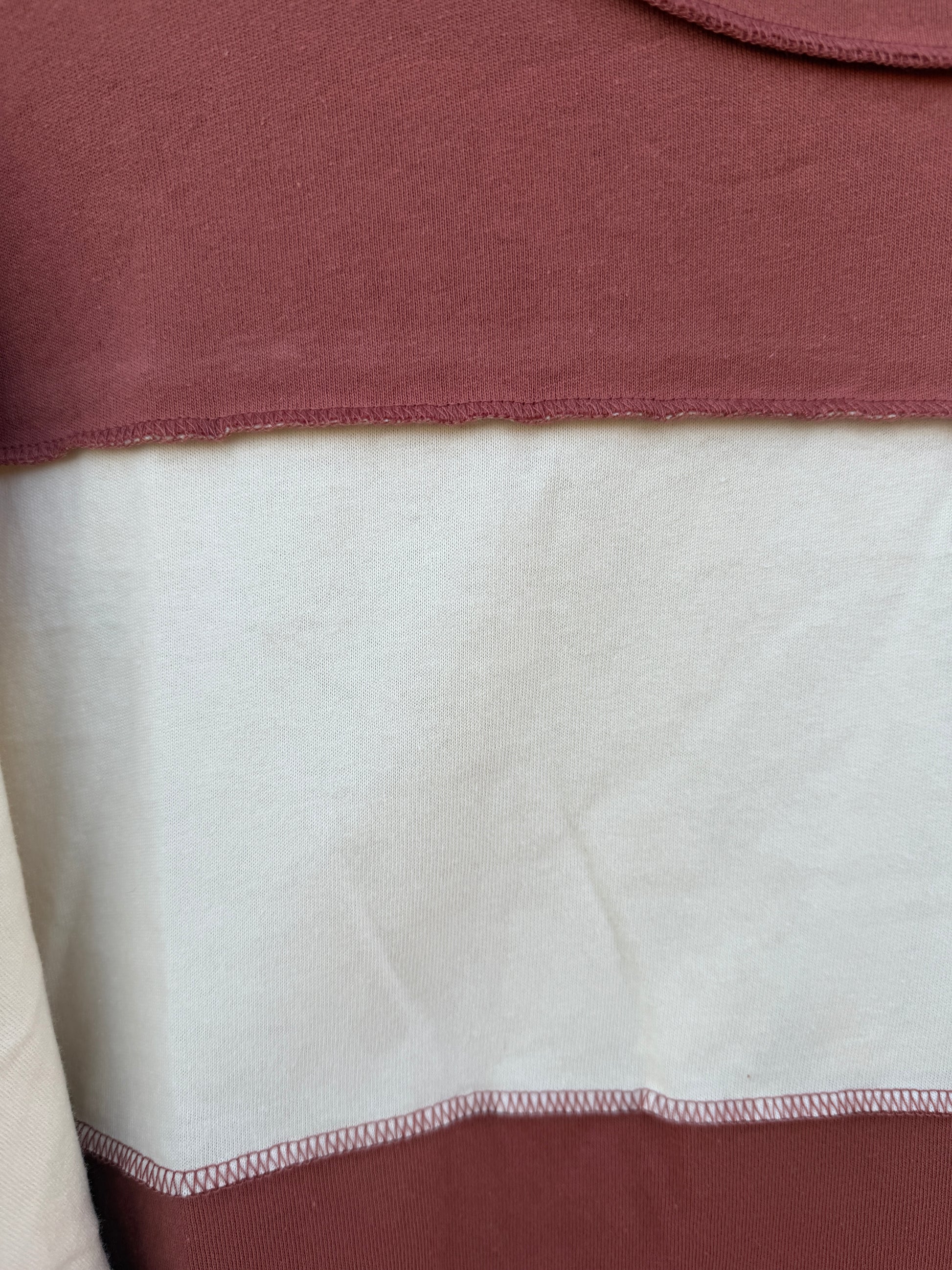 Close-up of a color-blocked garment showing a dusty rose/mauve top section, a large off-white central panel, and a darker mauve bottom section with visible stitched seams.