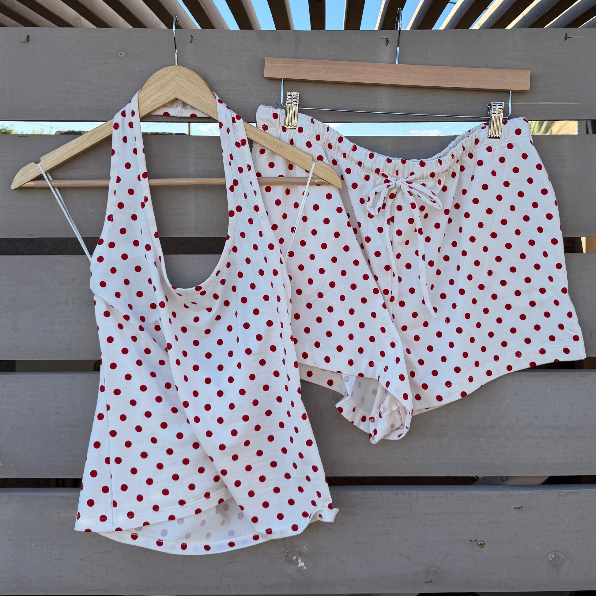 White polka dot top and shorts hanging on a wooden rack against a blue sky.