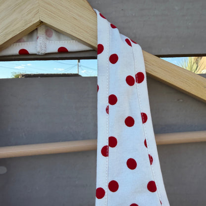 White tank with red polka dots on a wooden hanger against a neutral background