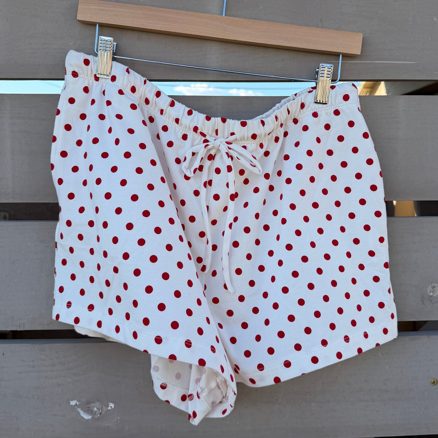 White shorts with red polka dots hanging on a clothesline against a wooden fence.