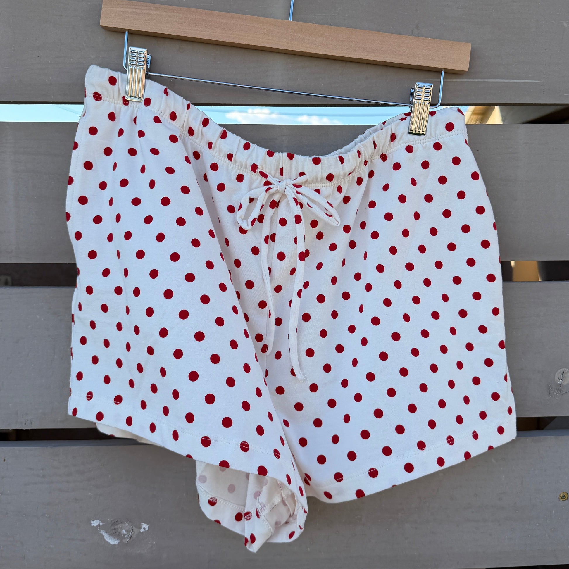 White shorts with red polka dots hanging on a clothesline against a wooden fence.