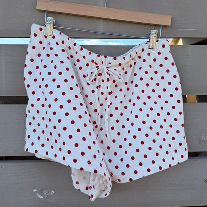 White shorts with red polka dots hanging on a clothesline against a wooden fence.
