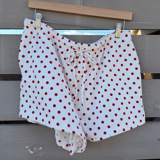 White shorts with red polka dots hanging on a clothesline against a wooden fence.