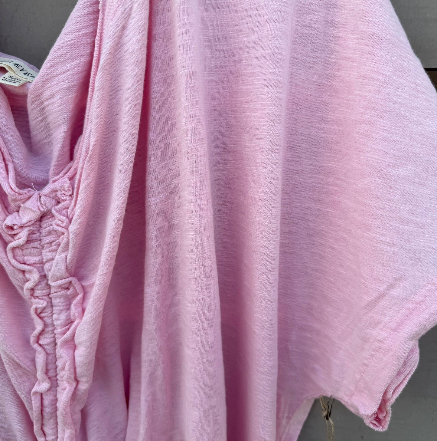 A light pink crinkled cotton kaftan or tunic top draped over a hanger, showing its textured fabric and gathered side details.