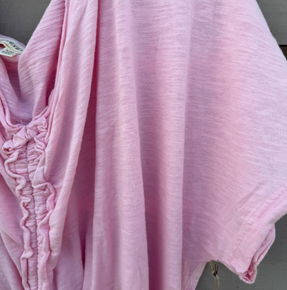 A light pink crinkled cotton kaftan or tunic top draped over a hanger, showing its textured fabric and gathered side details.