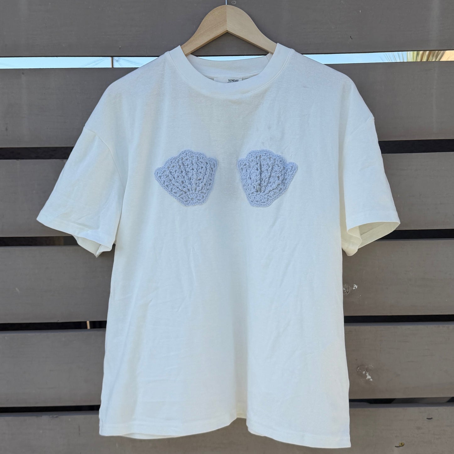 White t-shirt with blue shell patterns on a wooden background
