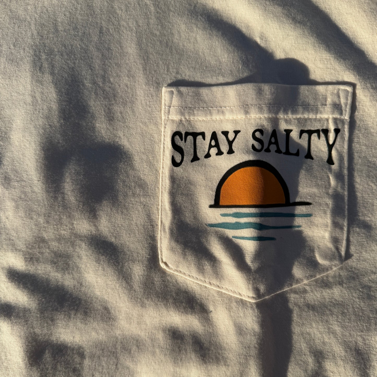Cream shirt with a pocket featuring 'Stay Salty' text and graphic.