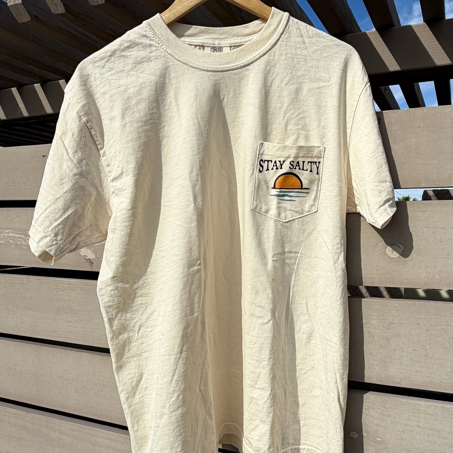 White t-shirt with a logo on a wooden surface against a blue sky