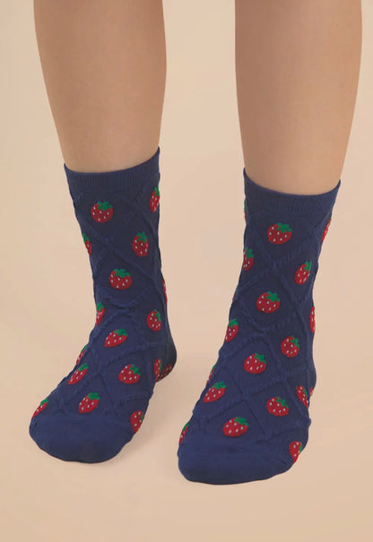 Blue socks with strawberry pattern worn by a person on a beige background
