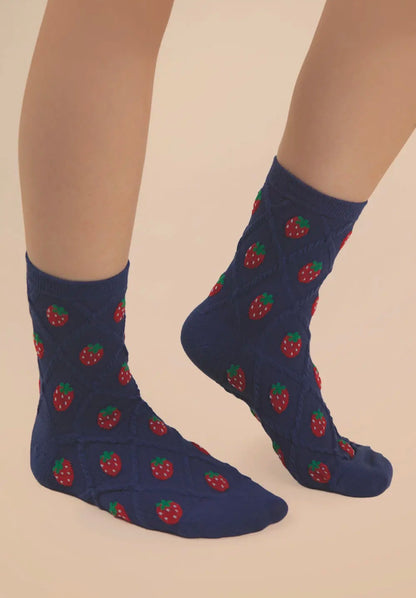 Navy blue socks with red strawberry pattern worn by a person on a beige background
