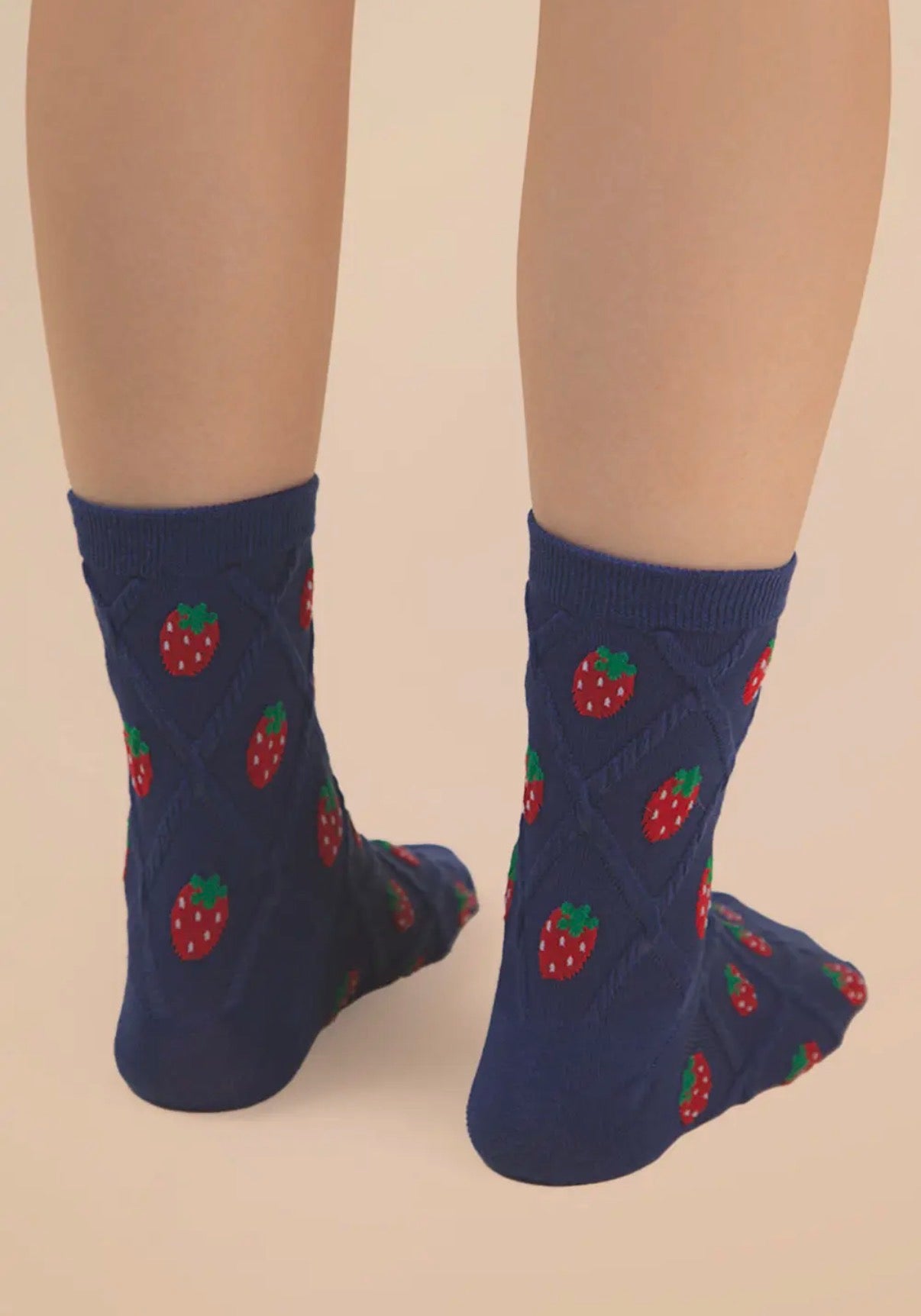 Navy blue socks with strawberry pattern worn by a person on a beige background