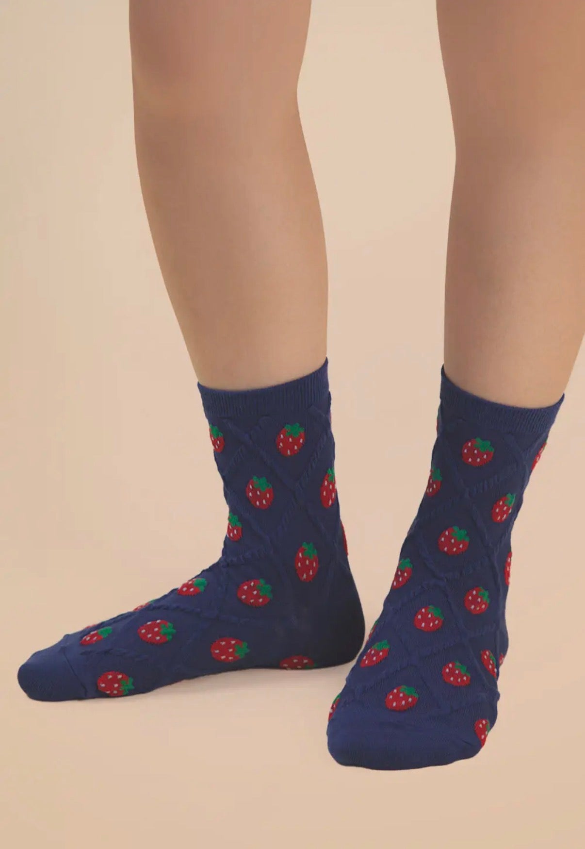 Navy blue socks with red strawberry pattern worn by a person on a beige background